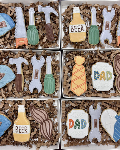 Collection of cookies shaped like tools, bottles, and 'DAD' text in a box.