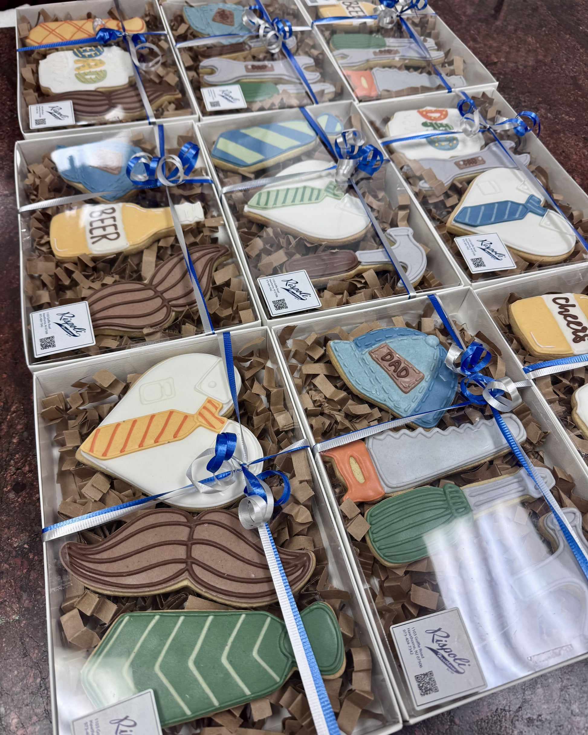Decorative cookies shaped like various items in a box with blue ribbons.