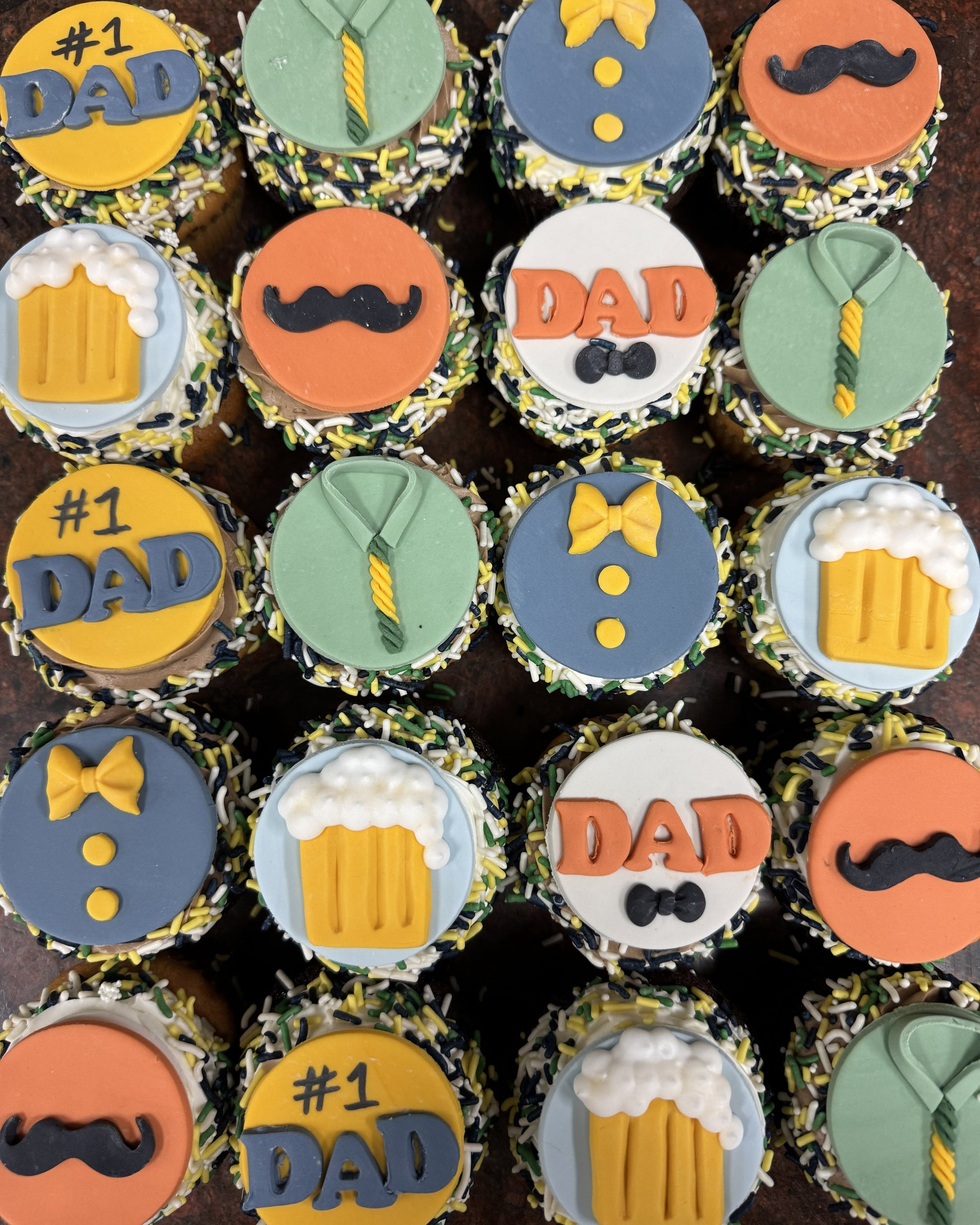 Cupcakes decorated with father-themed designs including ties, beer mugs, and mustaches on a dark background.