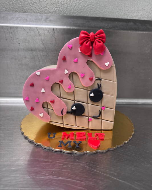 Heart-shaped cookie with a face, pink icing, and red bow on a metallic surface.