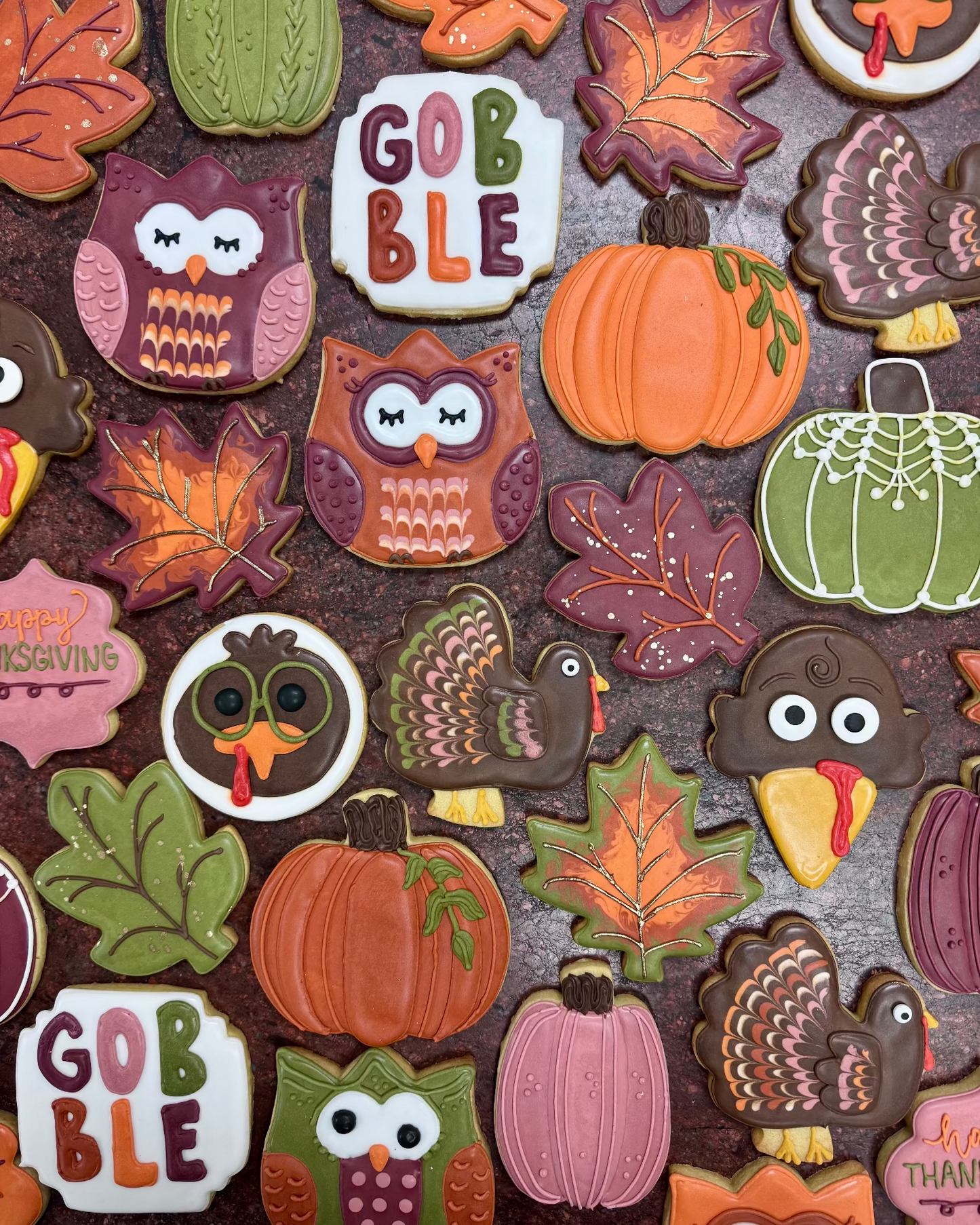 Collection of colorful fall-themed cookies including owls, pumpkins, and leaves on a dark surface.