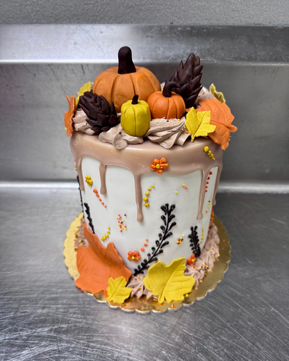 Fall-themed cake with pumpkins, leaves, and chocolate drizzle on a metallic surface