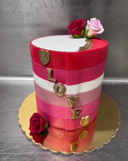 Decorative cake with red, white, and gold colors, featuring roses and 'LOVE' letters on a metallic surface.