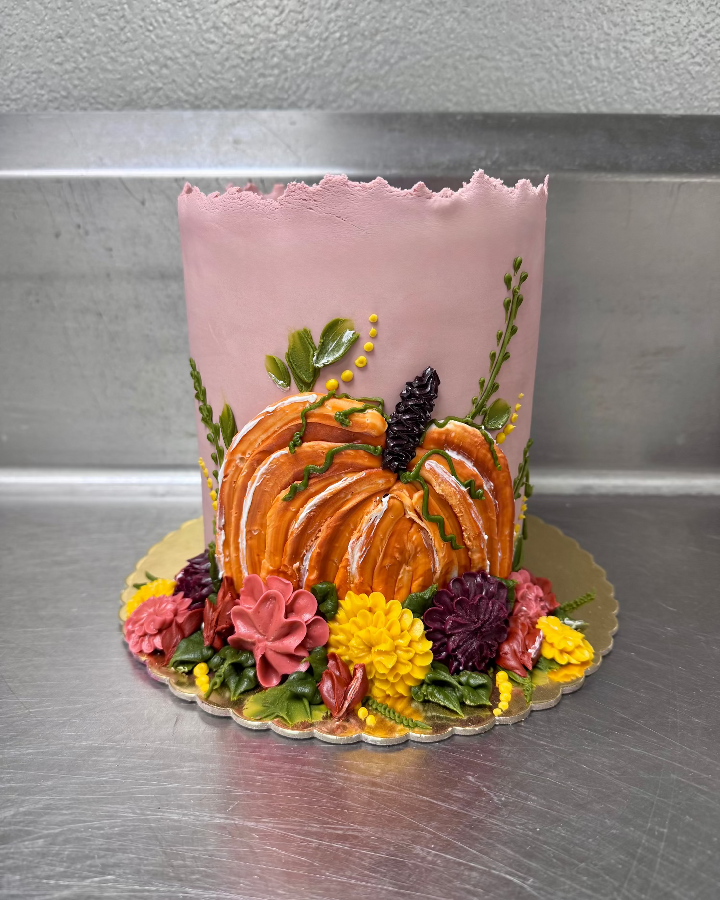 Decorative cake with pink frosting, pumpkin, and flowers on a metallic surface