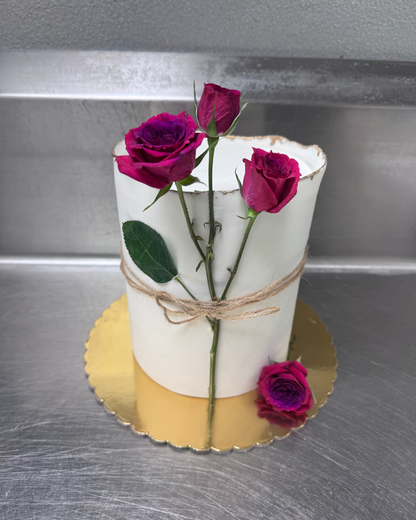White cake with fresh roses on a metallic surface