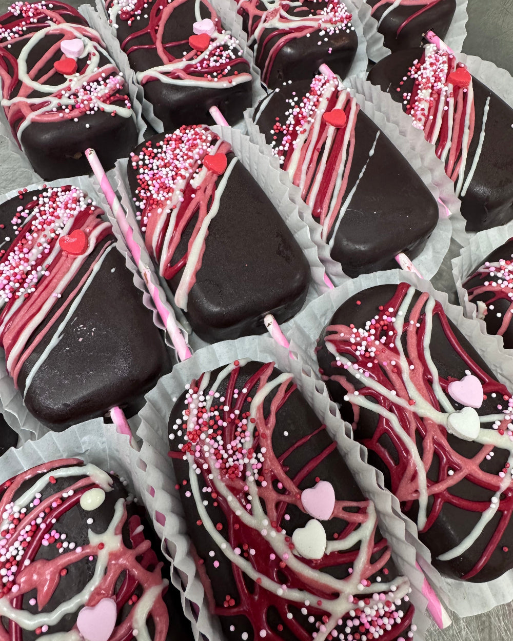 Assorted chocolate covered treats with pink and white drizzle and sprinkles in a box.