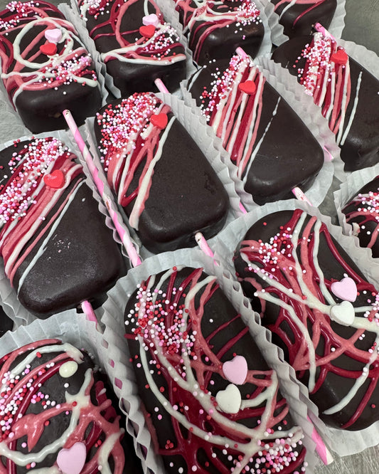 Assorted chocolate covered treats with pink and white drizzle and sprinkles in a box.