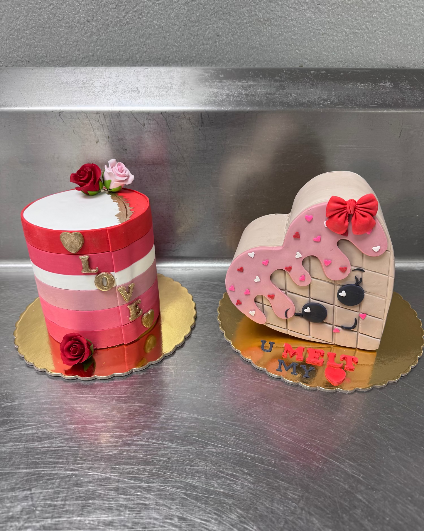 Two decorative cakes, one shaped like a heart with a face and the other cylindrical with floral decorations.