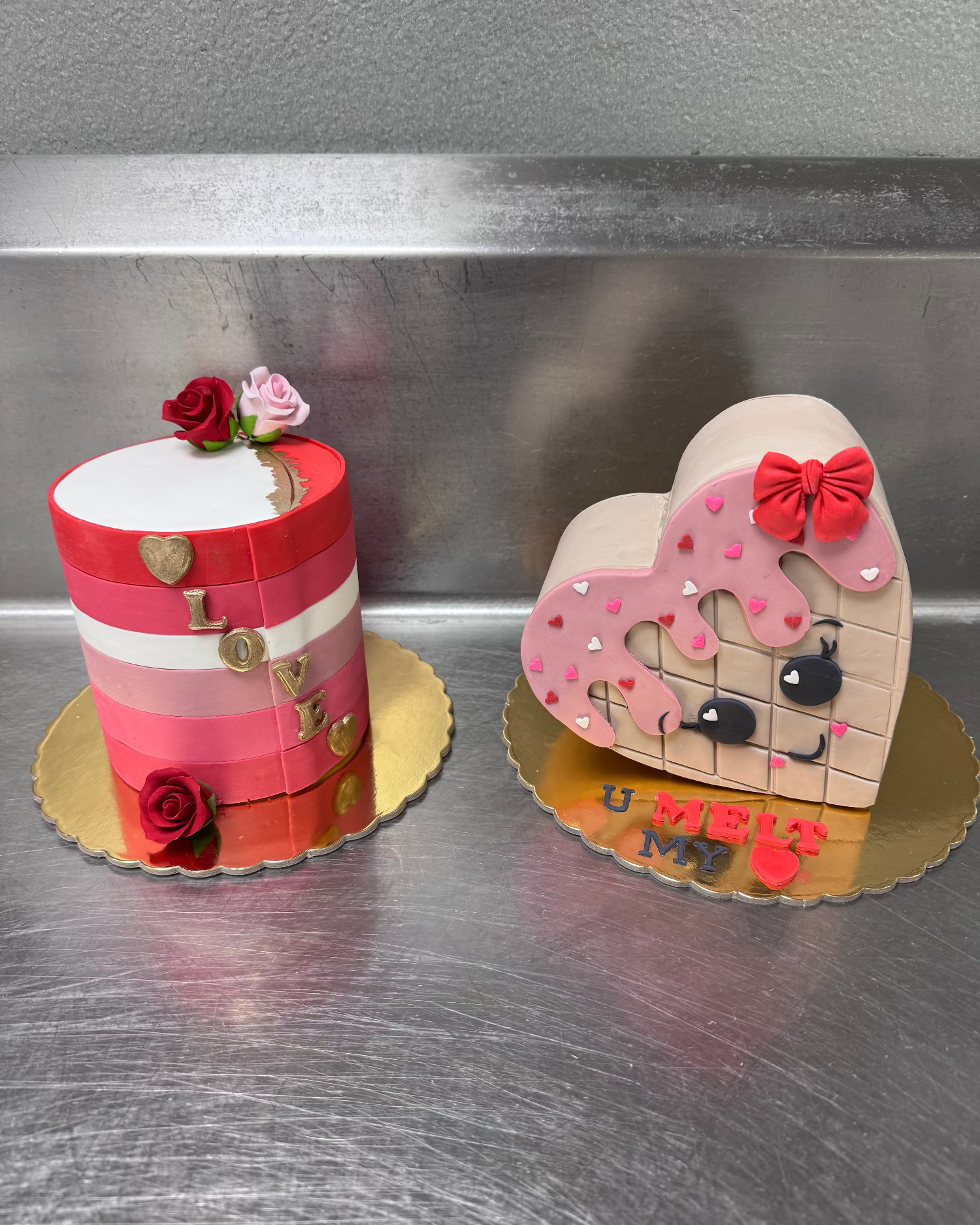Two decorative cakes, one shaped like a heart with a face and the other cylindrical with floral decorations.