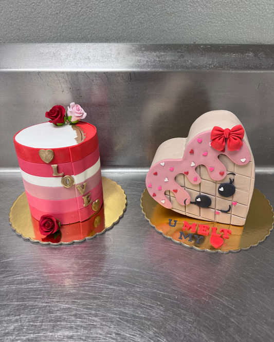 Two decorative cakes, one shaped like a heart with a face and the other cylindrical with floral decorations.