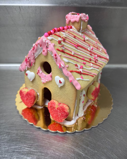 Decorative gingerbread house with pink and red icing on a metallic surface