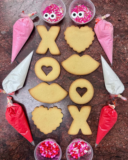 Decorative cookies shaped like lips, hearts, and 'XO' on a brown surface with icing bags and sprinkles.
